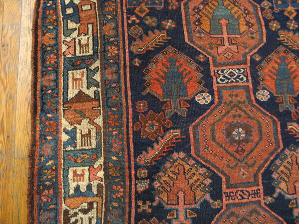 Navy blue rug with rust geometric medallions and detailed borders rests on light hardwood flooring.