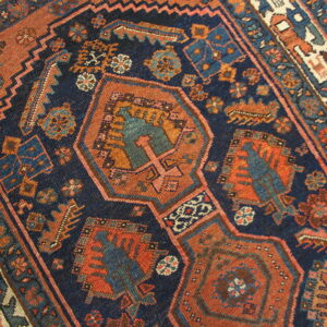 Deep indigo and rust-orange geometric rug detail showing a central medallion and patterned border on a wood floor.