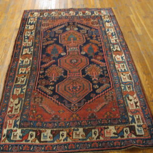 Navy and rust geometric rug featuring small animal motifs in the border, displayed on hardwood flooring.