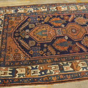 Navy and rust traditional rug featuring geometric designs and multiple borders on light wood flooring.