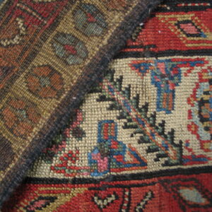 Two intricately woven rugs overlap, displaying geometric motifs in deep red, cream, blue, and earth tones.