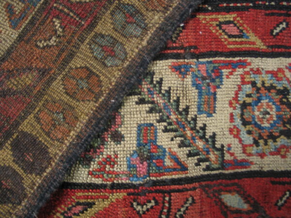 Two intricately woven rugs overlap, displaying geometric motifs in deep red, cream, blue, and earth tones.