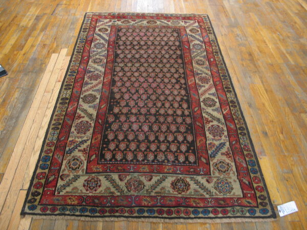 Rectangular rug with a dark field, red paisley motifs, and multi-colored borders rests on wood planks.