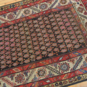 Red, black, and cream low-pile rug featuring a field of repeating geometric shapes and a multi-banded border.