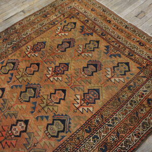 Geometric rust and navy rug with a detailed border, displayed on wide, distressed gray wood floor.