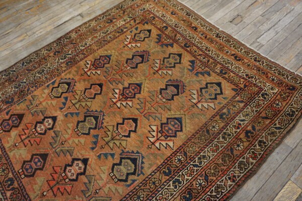 Geometric rust and navy rug with a detailed border, displayed on wide, distressed gray wood floor.