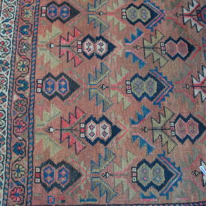 Repeating dark navy and olive geometric motifs on a rust-colored rug field with a contrasting floral border.