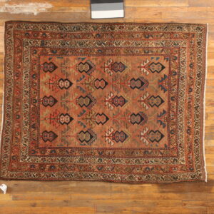 Low-pile rug featuring rust and multicolored geometric motifs with ornate borders on wood flooring.