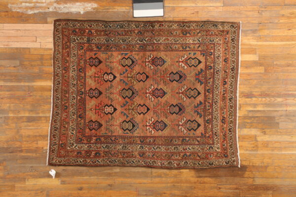 Low-pile rug featuring rust and multicolored geometric motifs with ornate borders on wood flooring.