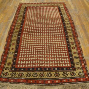 A rustic red and beige rug with a dense diamond field and geometric borders rests on distressed wood planks.