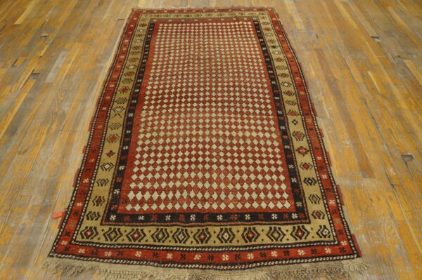 A rustic red and beige rug with a dense diamond field and geometric borders rests on distressed wood planks.