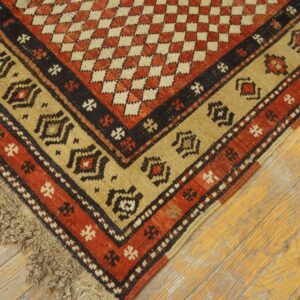 Close view of a coarse, low-pile rug in rust red, tan, and black on distressed hardwood planks.