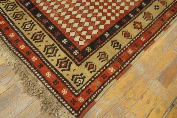 Close view of a coarse, low-pile rug in rust red, tan, and black on distressed hardwood planks.