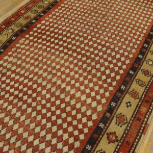 Rust and beige geometric rug featuring a checkerboard field and patterned outer borders on wood floor.