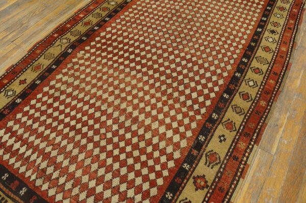 Rust and beige geometric rug featuring a checkerboard field and patterned outer borders on wood floor.