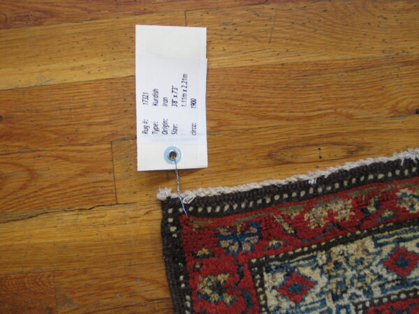 High-pile corner of a red, blue, and cream geometric rug on distressed hardwood flooring.