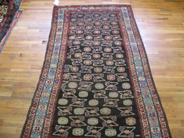 Dark brown runner rug with complex red, blue, and tan geometric motifs on light wood floors.