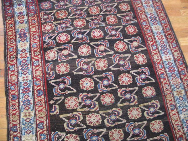 Dark brown geometric rug with repeating red, blue, and cream medallions and complex striped borders on wood flooring.