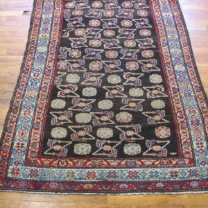 Dark geometric runner rug featuring repeating cream, red, and blue motifs laid on worn wood floorboards.