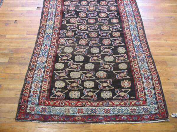 Dark geometric runner rug featuring repeating cream, red, and blue motifs laid on worn wood floorboards.