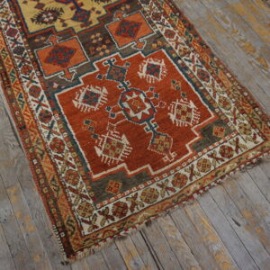 A rust and yellow low pile rug with complex geometric patterns rests on distressed gray wood planks.