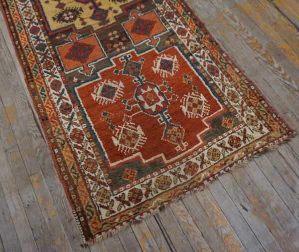 A rust and yellow low pile rug with complex geometric patterns rests on distressed gray wood planks.