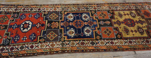 Colorful geometric runner rug with complex red, blue, and gold tribal patterns on wood planks.