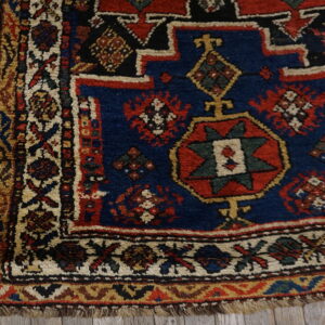 Geometric, high-pile rug corner featuring blue, red, and cream designs on light gray wood planks.
