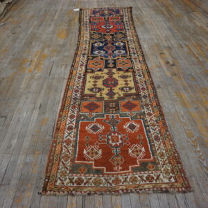 Multi-colored geometric runner rug featuring orange, navy, and gold panels on distressed wood planks.