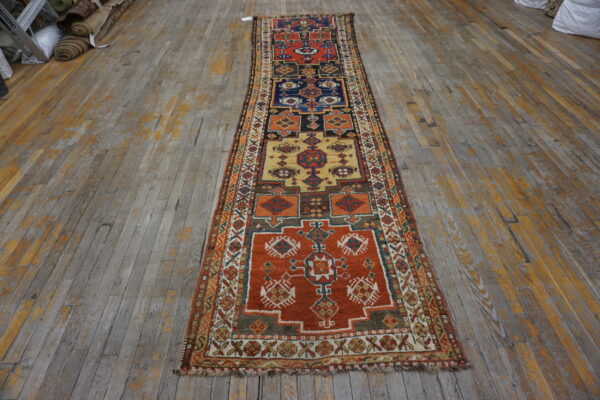 Multi-colored geometric runner rug featuring orange, navy, and gold panels on distressed wood planks.