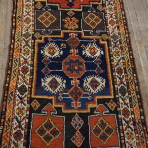 Geometric runner rug with repeating motifs in navy, rust, and black lays on distressed wooden planks.