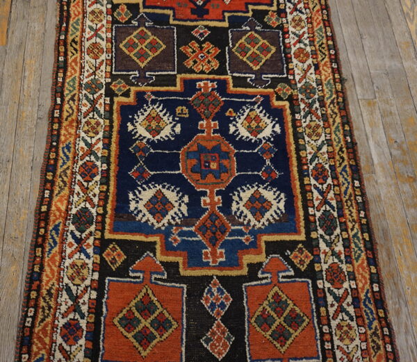 Geometric runner rug with repeating motifs in navy, rust, and black lays on distressed wooden planks.