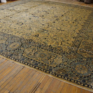 Oversized golden yellow and blue floral rug with complex borders rests on rustic wood flooring.