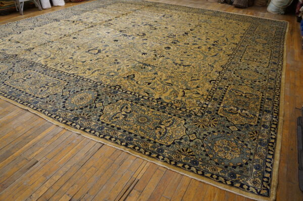 Oversized golden yellow and blue floral rug with complex borders rests on rustic wood flooring.