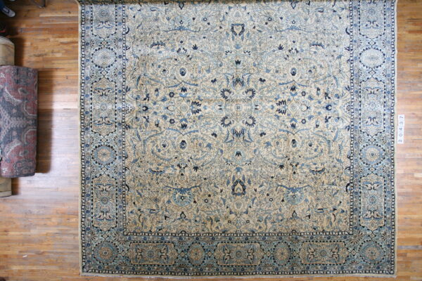 Traditional cream rug with intricate light and deep blue floral designs flat on warm wood flooring.