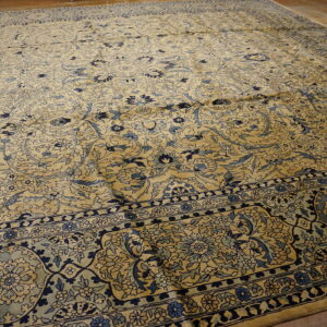 Intricate floral area rug in gold and shades of blue lying on a polished wood floor.