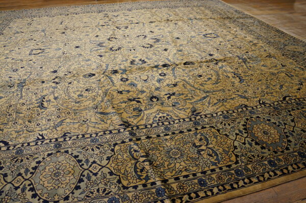 Intricate floral area rug in gold and shades of blue lying on a polished wood floor.
