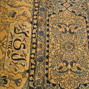 Detailed view of a golden yellow rug featuring dense blue floral motifs, ornamental borders, and dark calligraphy script.