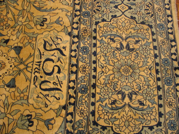 Detailed view of a golden yellow rug featuring dense blue floral motifs, ornamental borders, and dark calligraphy script.