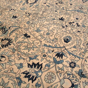 Low-pile rug detailed with intricate blue floral and vine motifs on a light beige background.