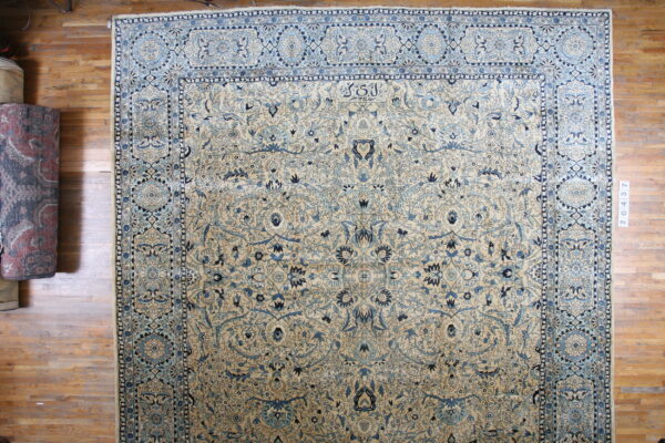 A large cream rug with intricate blue floral borders and vines rests on wood planks.