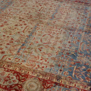 Distressed traditional rug showing red floral patterns on alternating blue and faded beige fields with red borders.