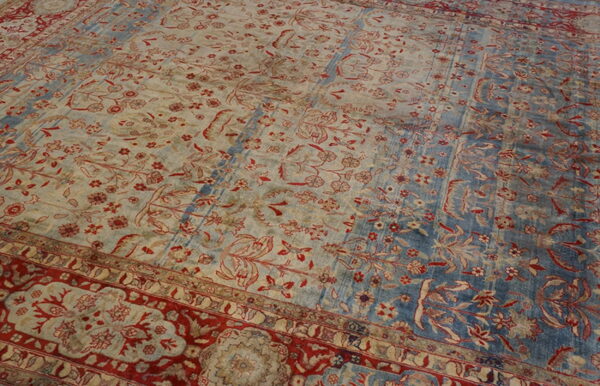 Distressed traditional rug showing red floral patterns on alternating blue and faded beige fields with red borders.