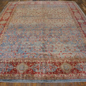 A large pale blue and red ornate rug with a dense pattern rests on glossy wood planks.