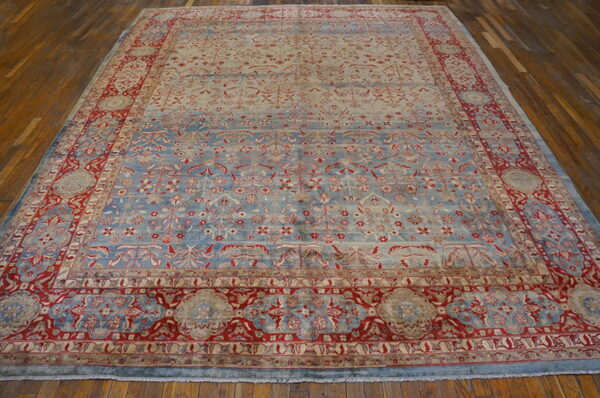 A large pale blue and red ornate rug with a dense pattern rests on glossy wood planks.