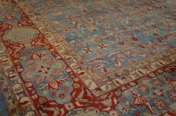 Low-pile rug detail showing intricate red and beige floral motifs on a light blue background.