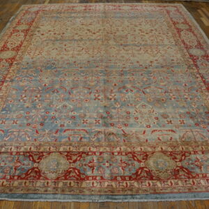 Low-pile rug in light blue and cream with intricate red floral patterns rests on a brown hardwood floor.