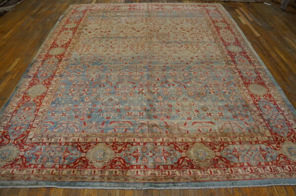 Low-pile rug in light blue and cream with intricate red floral patterns rests on a brown hardwood floor.
