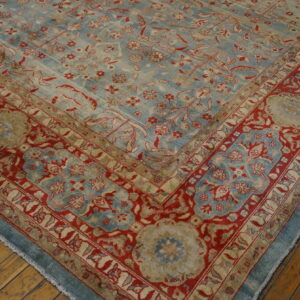 A corner view of a traditional blue, red, and tan floral rug on wooden flooring.