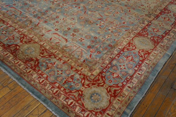 A corner view of a traditional blue, red, and tan floral rug on wooden flooring.
